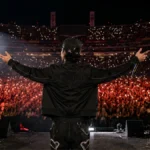 Imagen ilustrativa de un cantante de corridos tumbados de espaldas ante un estadio lleno
